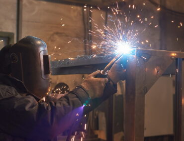 welder welds a metal frame for the power plant. The man works in a protective mask.
